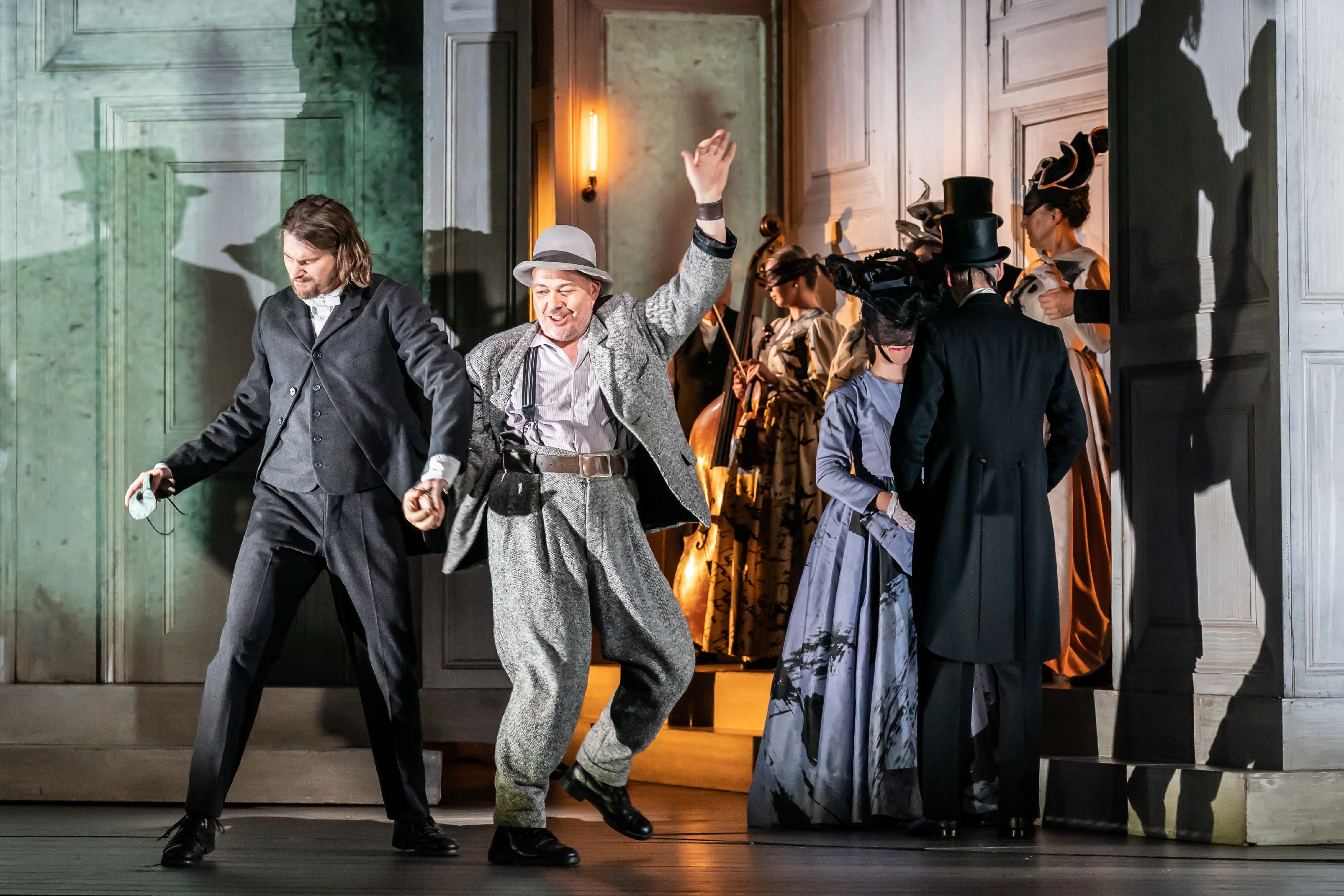 Several performers stand around a party scene in a traditionally decorated room on stage of The Royal Opera House in The Royal Opera's production of Don Giovanni. (3 of 4)
