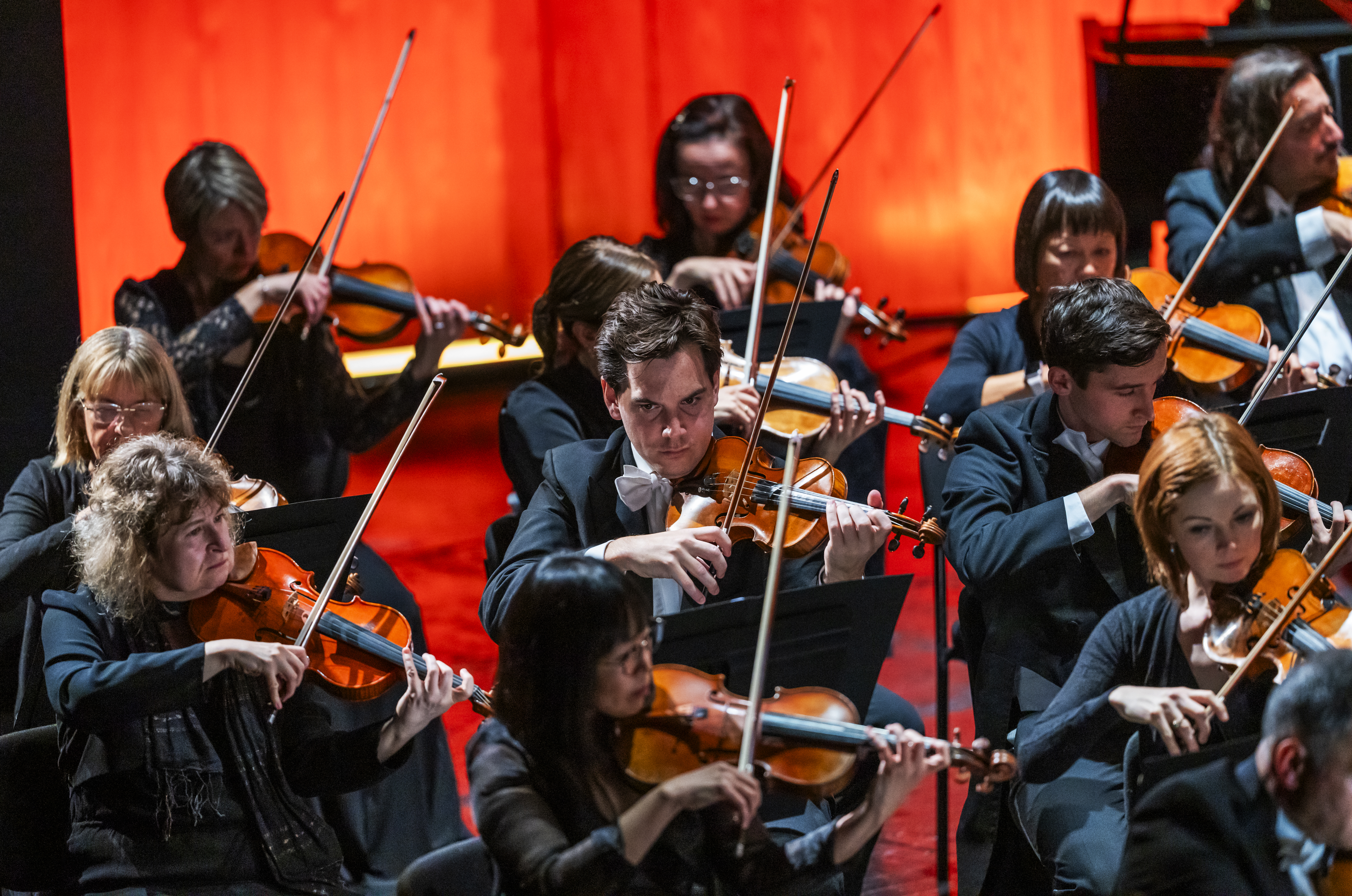 A group of violinists perform with their violinists on a brightly lit stage. (2 of 4)