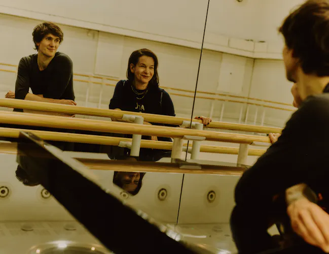 The choreographer Pam Tanowitz and The Royal Ballet dancer William Bracewell sit facing a mirrored wall against a barre in a well-lit dance studio. (4 of 10)