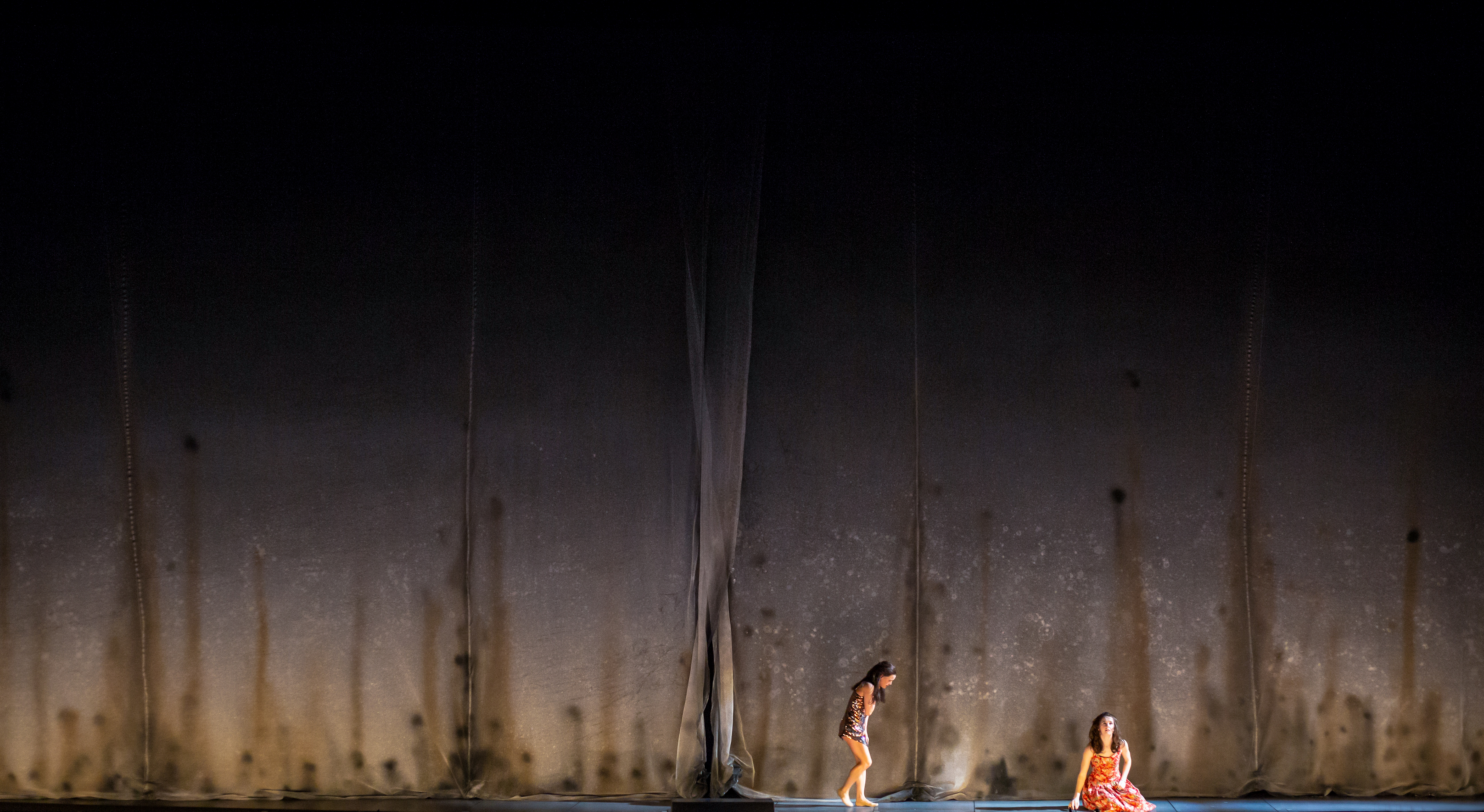 Two performers stand on dimly lit stage with a stark concrete backdrop. (3 of 6)