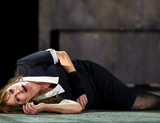 A performer wearing a black and white maids uniform lies on the stage looking out, almost in pain or turmoil. (5 of 5)