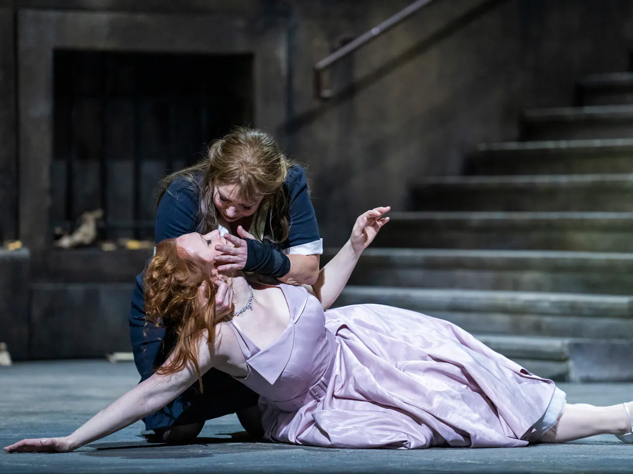 A performer wearing a black and white maids uniform holds the head up of a lifeless-looking performer wearing a purple dress.