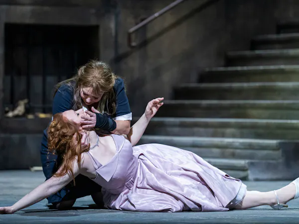 A performer wearing a black and white maids uniform holds the head up of a lifeless-looking performer wearing a purple dress.