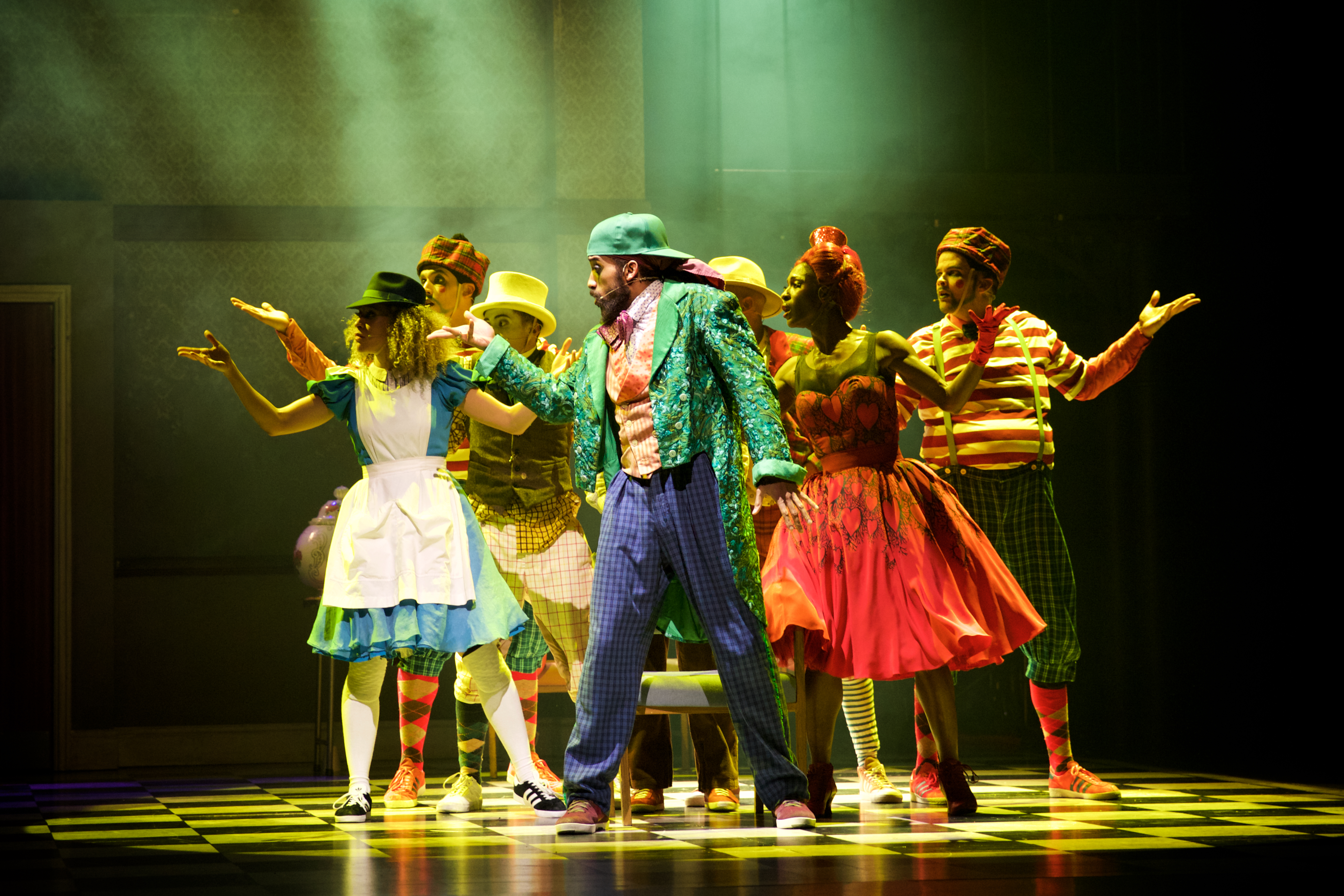 Several performers stand in the centre of a spotlight on a stage. They wear a variety of bright colour costumes. m (4 of 4)