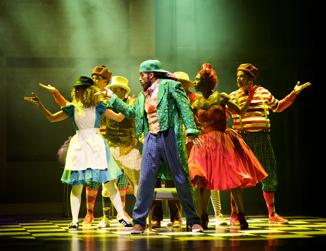 Several performers stand in the centre of a spotlight on a stage. They wear a variety of bright colour costumes. m (4 of 4)