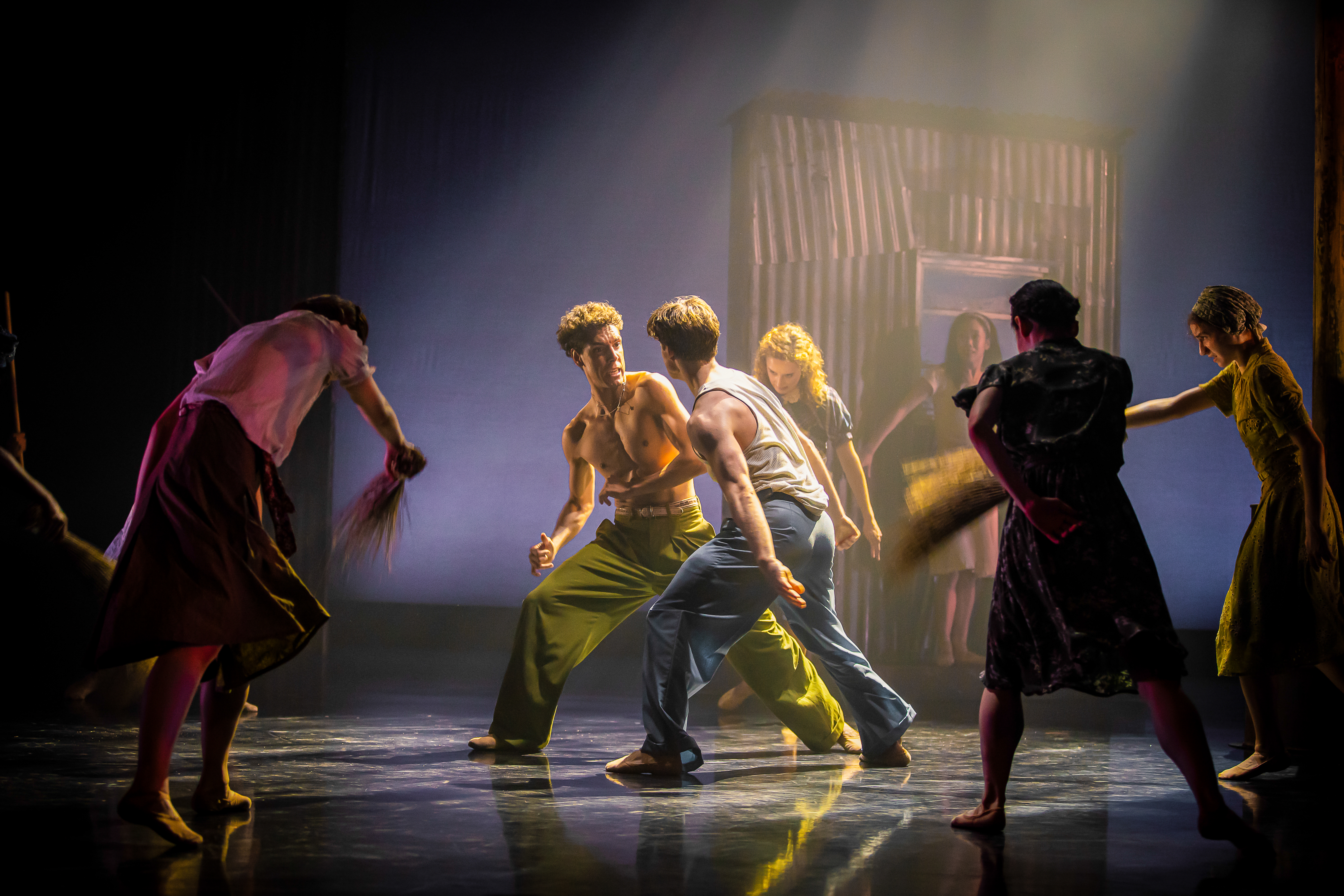 Several ballet dancers perform on stage in a dimly lit space with haze. 