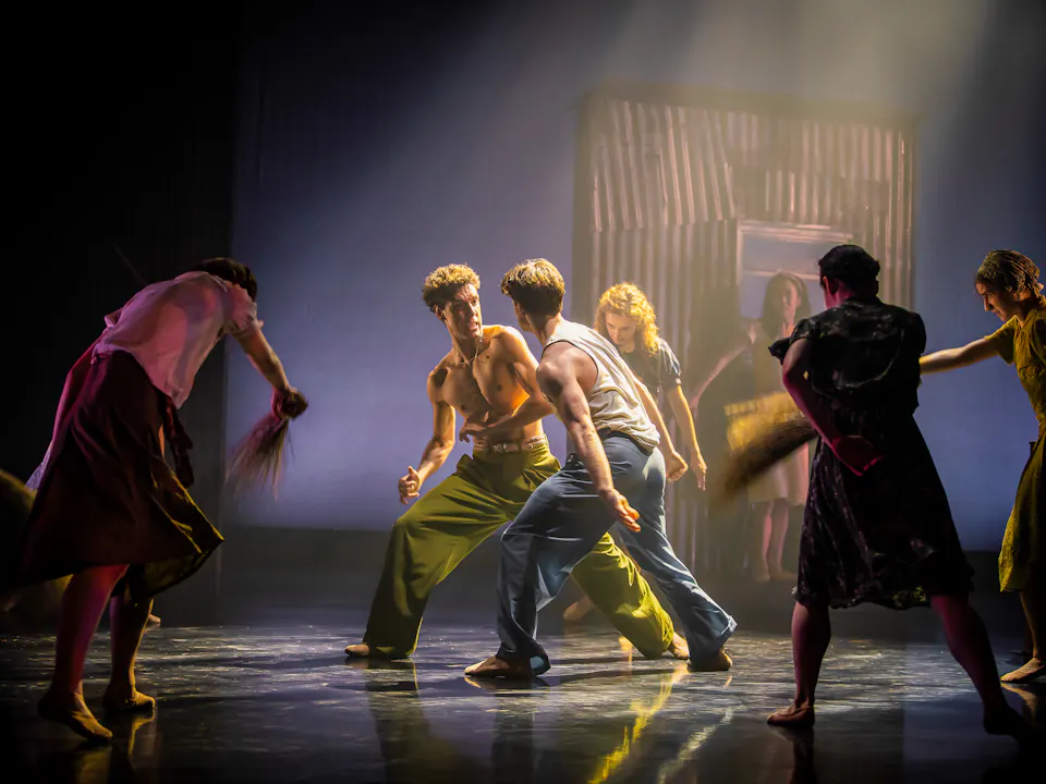 Several ballet dancers perform on stage in a dimly lit space with haze.