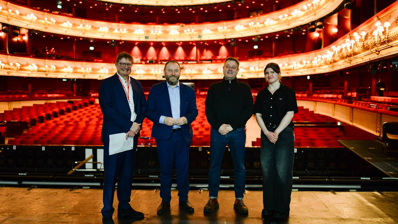 Four people stand together on stage, posing for a photo. Behind them is the grand Royal Opera House auditorium.