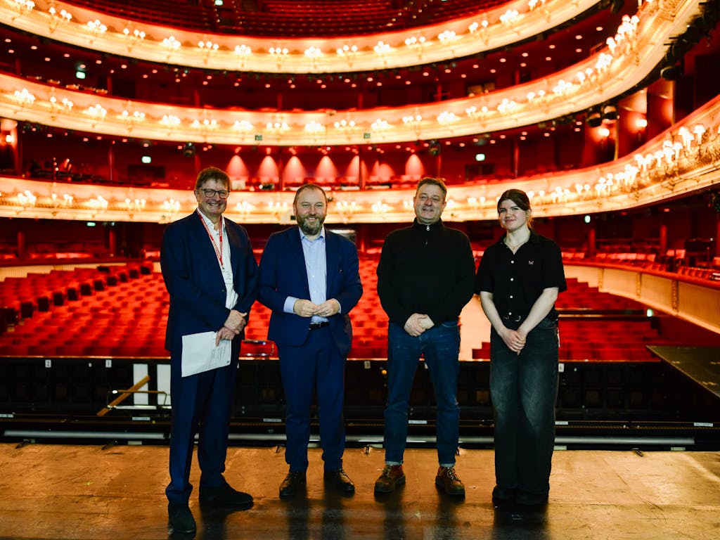 Four people stand together on stage, posing for a photo. Behind them is the grand Royal Opera House auditorium.