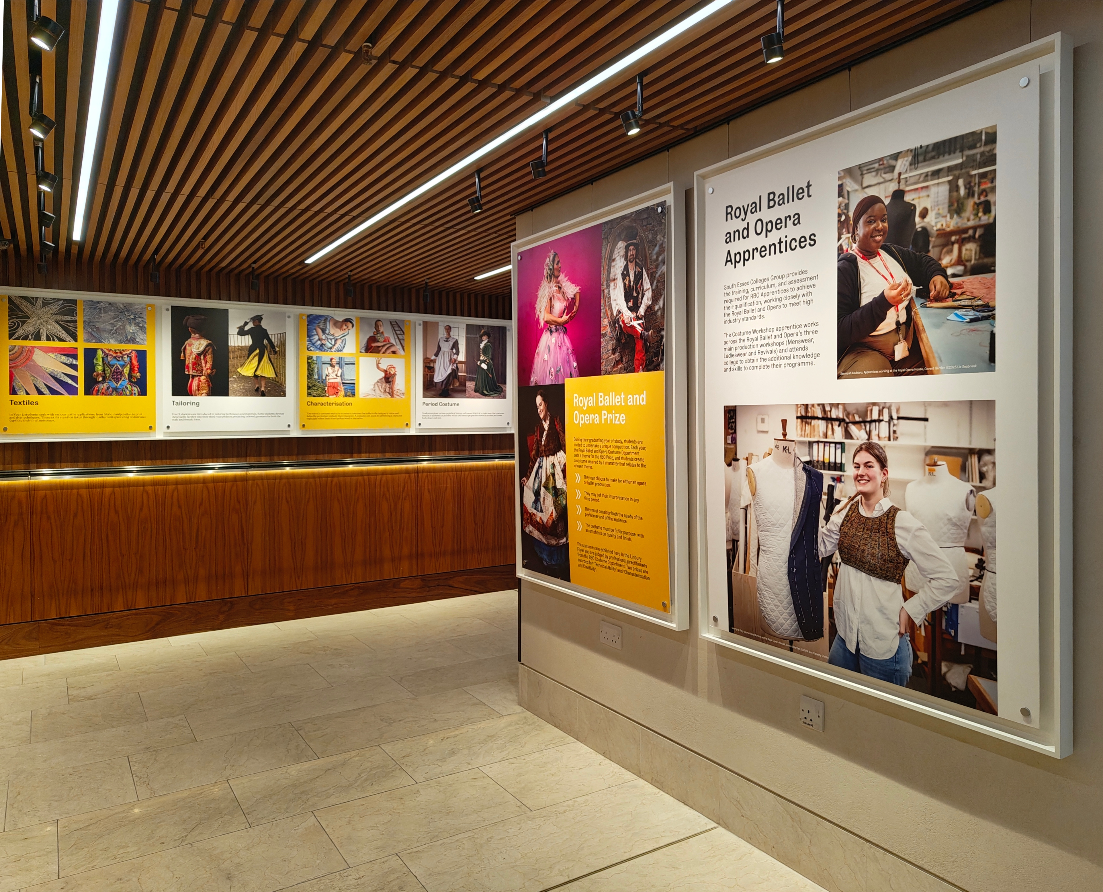 A modern gallery space with wooden ceiling panels, large framed photos and text about the Royal Ballet and Opera Prize on the walls. 