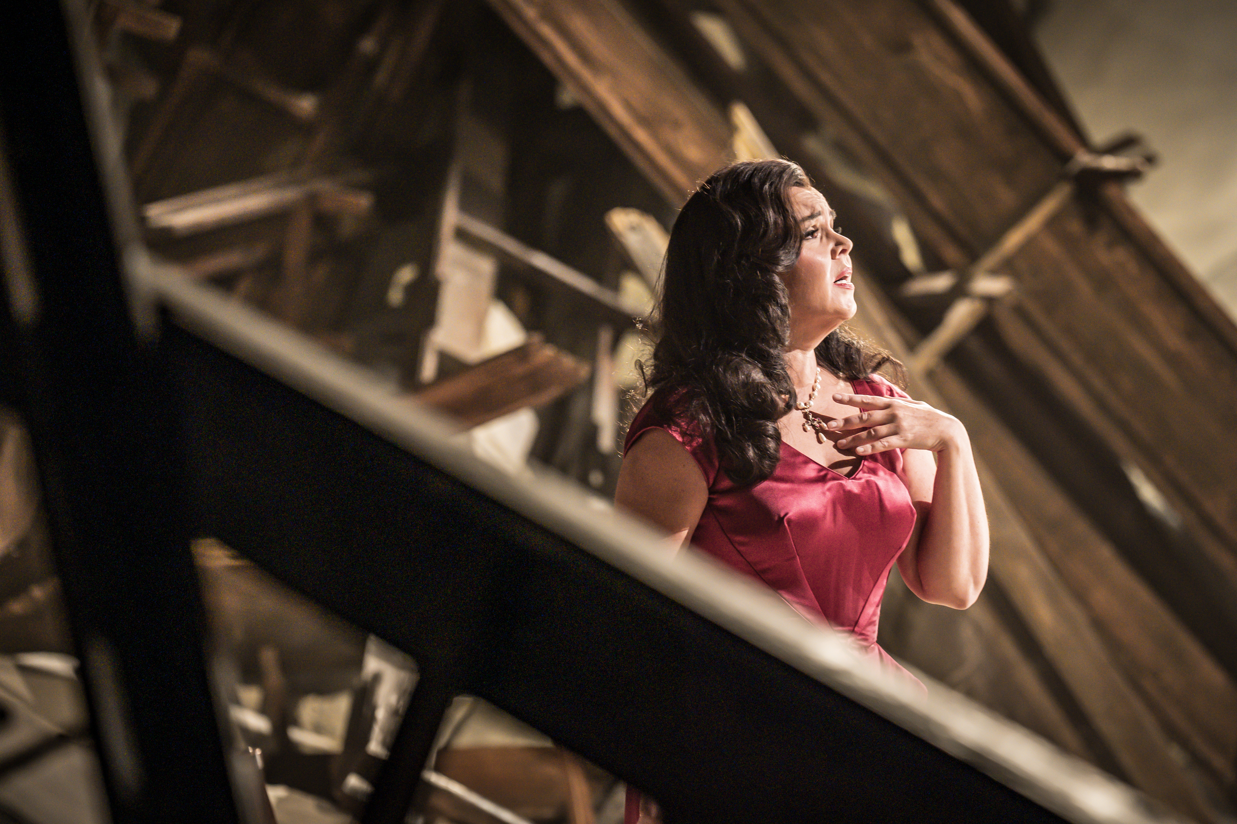 Aleksandra Kurzak playing Floria Tosca stands in a red dress stands amidst debris from a bombed out church.
