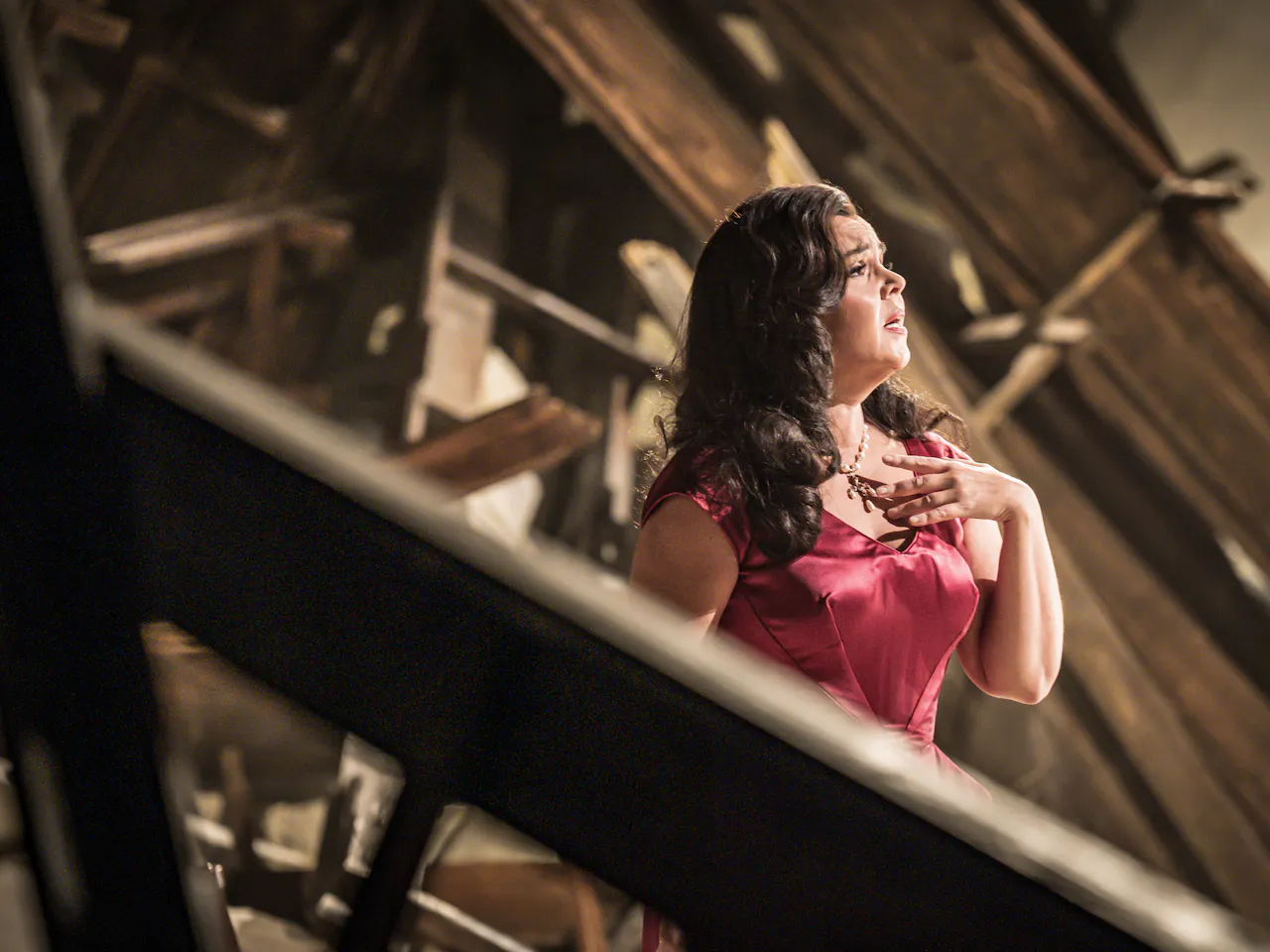 Aleksandra Kurzak playing Floria Tosca stands in a red dress stands amidst debris from a bombed out church.