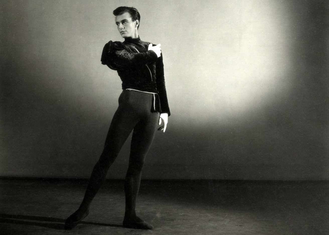 A black and white studio portrait photograph of the choreographer Peter Wright in 1951. He stands wearing black leotard and black top. 