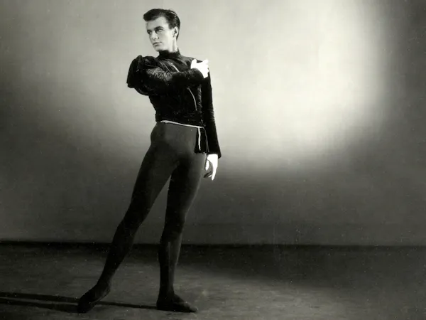 A black and white studio portrait photograph of the choreographer Peter Wright in 1951. He stands wearing black leotard and black top.