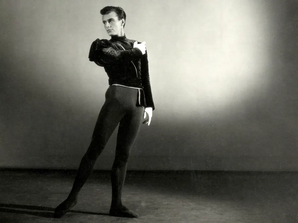 A black and white studio portrait photograph of the choreographer Peter Wright in 1951. He stands wearing black leotard and black top.