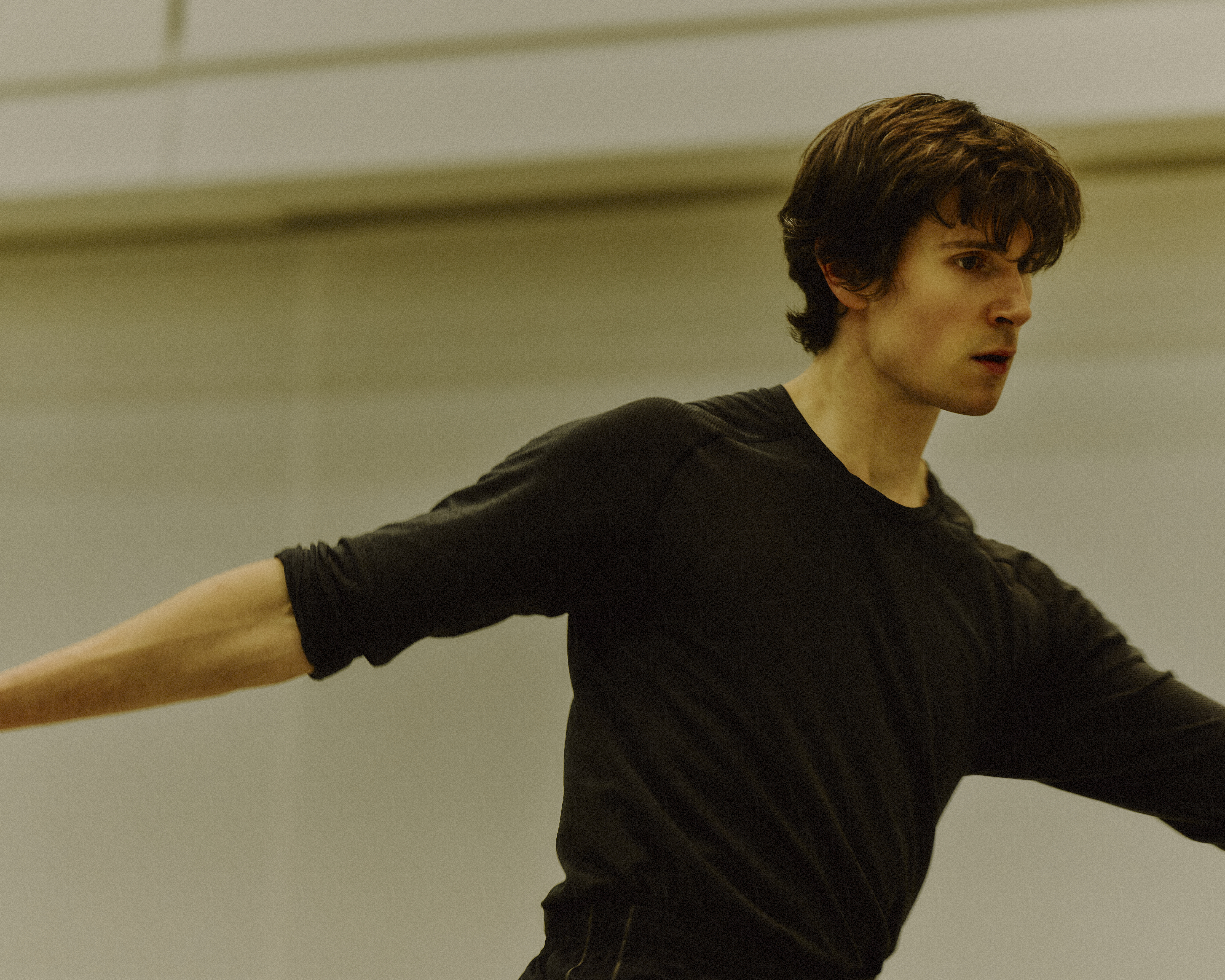 The Royal Ballet dancer William Bracewell performs in a well-lit dance studio in rehearsals with his arms stretched outwards. (2 of 4)