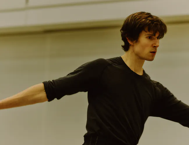 The Royal Ballet dancer William Bracewell performs in a well-lit dance studio in rehearsals with his arms stretched outwards. (2 of 4)