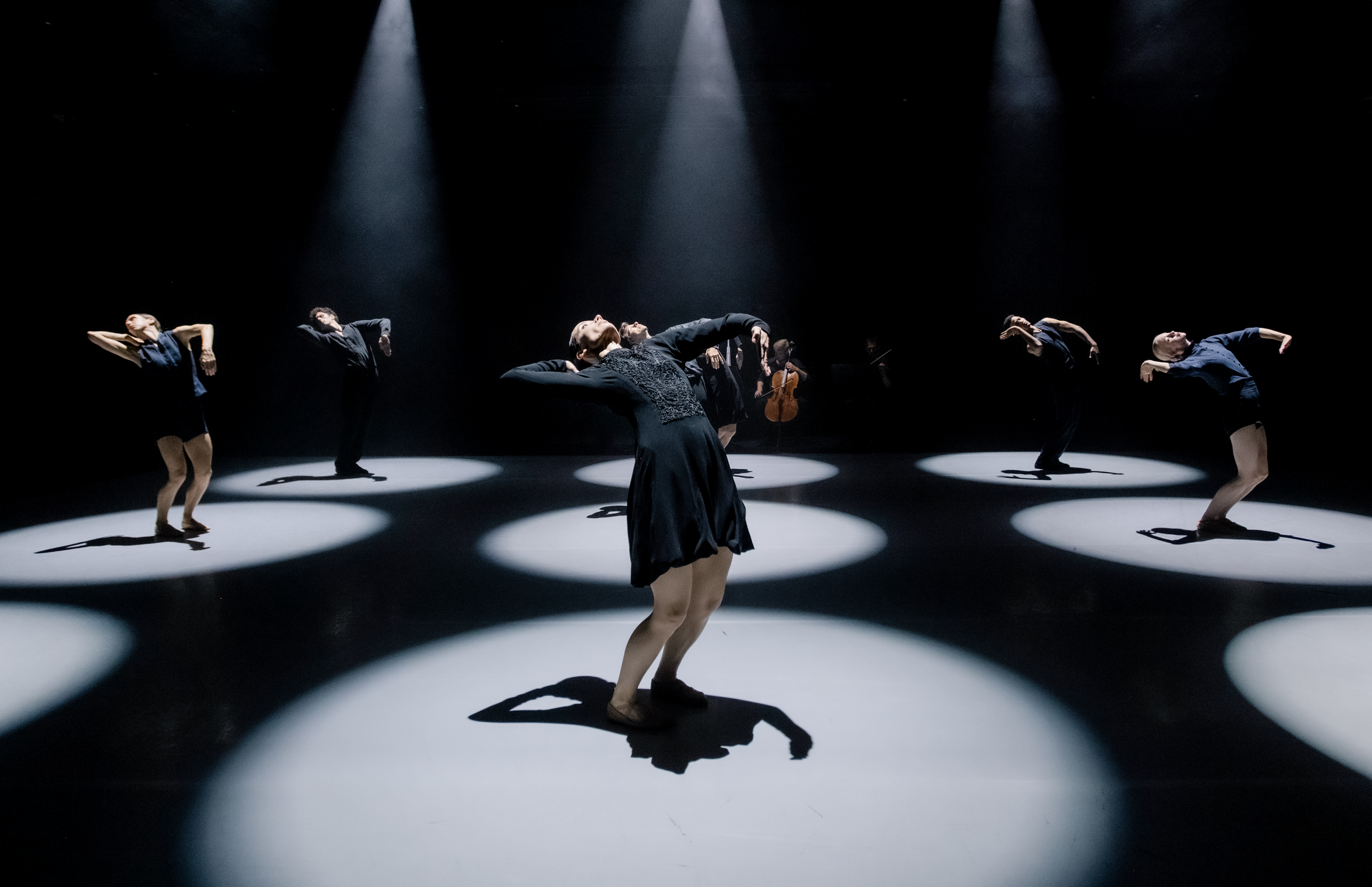 Several ballet dancers perform on a dark stage within a brightly lit circular spotlights. (7 of 10)