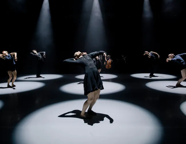 Several ballet dancers perform on a dark stage within a brightly lit circular spotlights. (7 of 10)