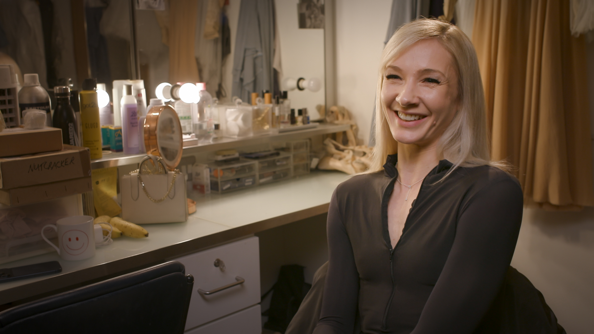 Melissa Hamilton sits in her dressing room, behind her is a large mirror with makeup and hair products.