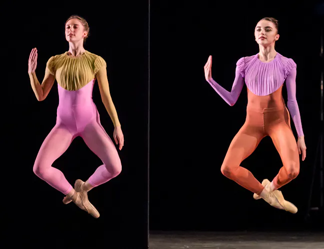 Artists of The Royal Ballet perform on a dark stage. Two dancers in colourful unitards are mid-jump. Their ankles are crossed and they all hold up their right arm. (4 of 5)