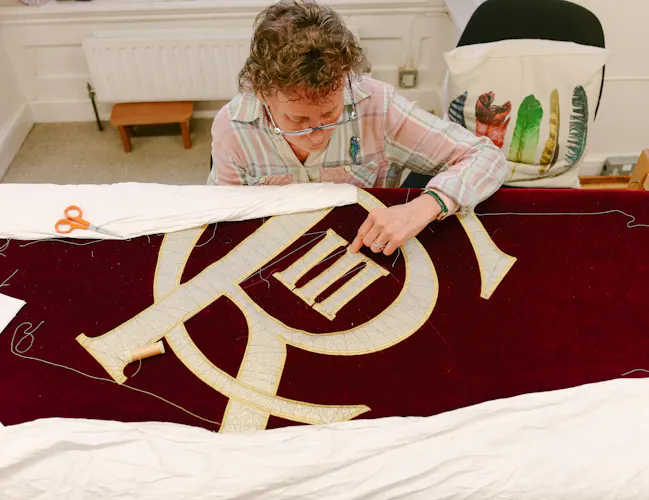 An embroiderer from the Royal School of Needlework sews King Charles III's insignia onto the new Royal Opera House stage curtains. (1 of 3)