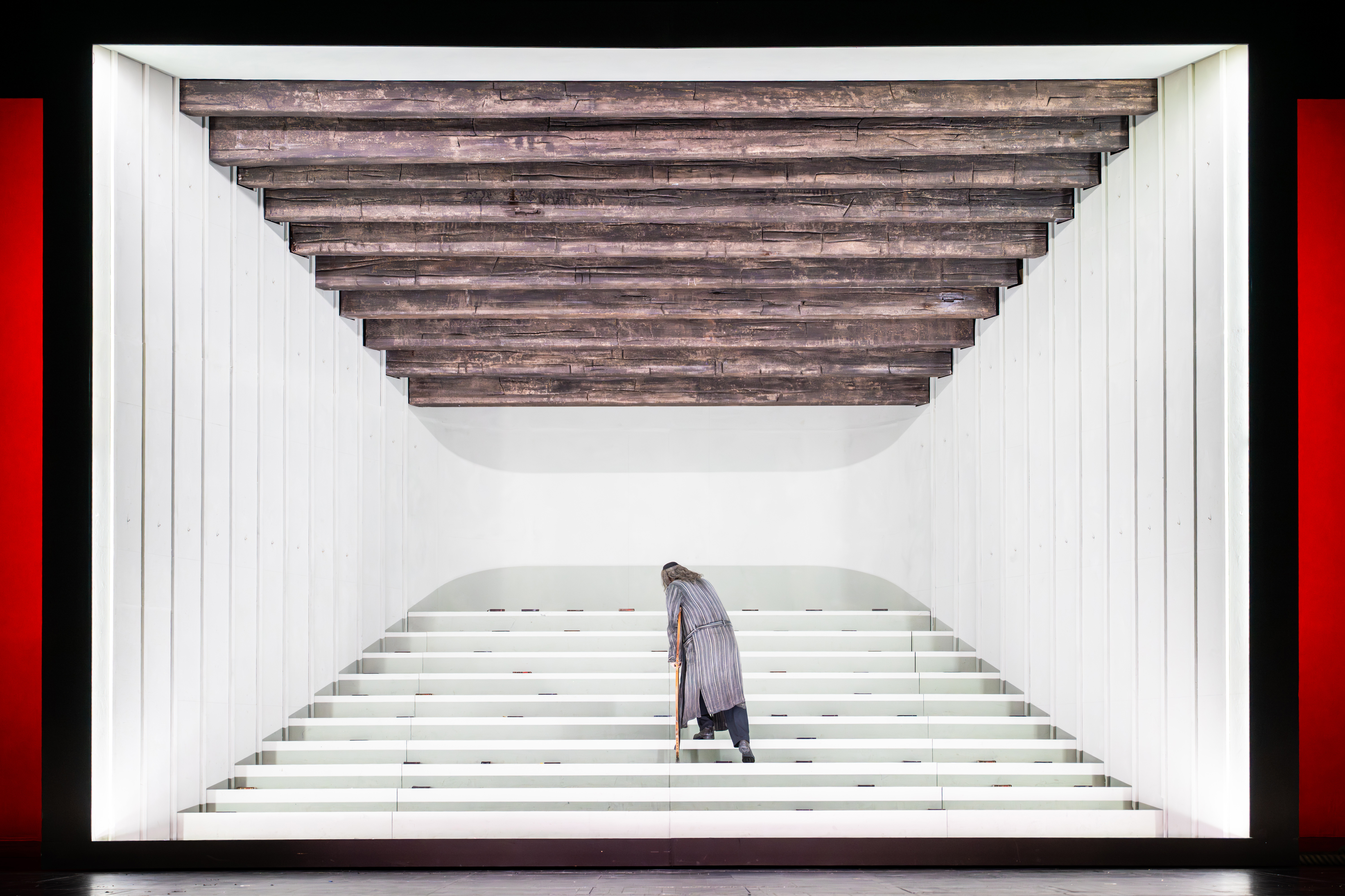 A man stands in a white box on a set of stairs. He has his back to the audience. (3 of 6)