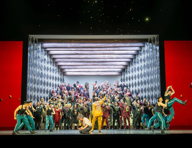 A large group of people in colourful outfits stand in and spill out of a small stage. (1 of 6)