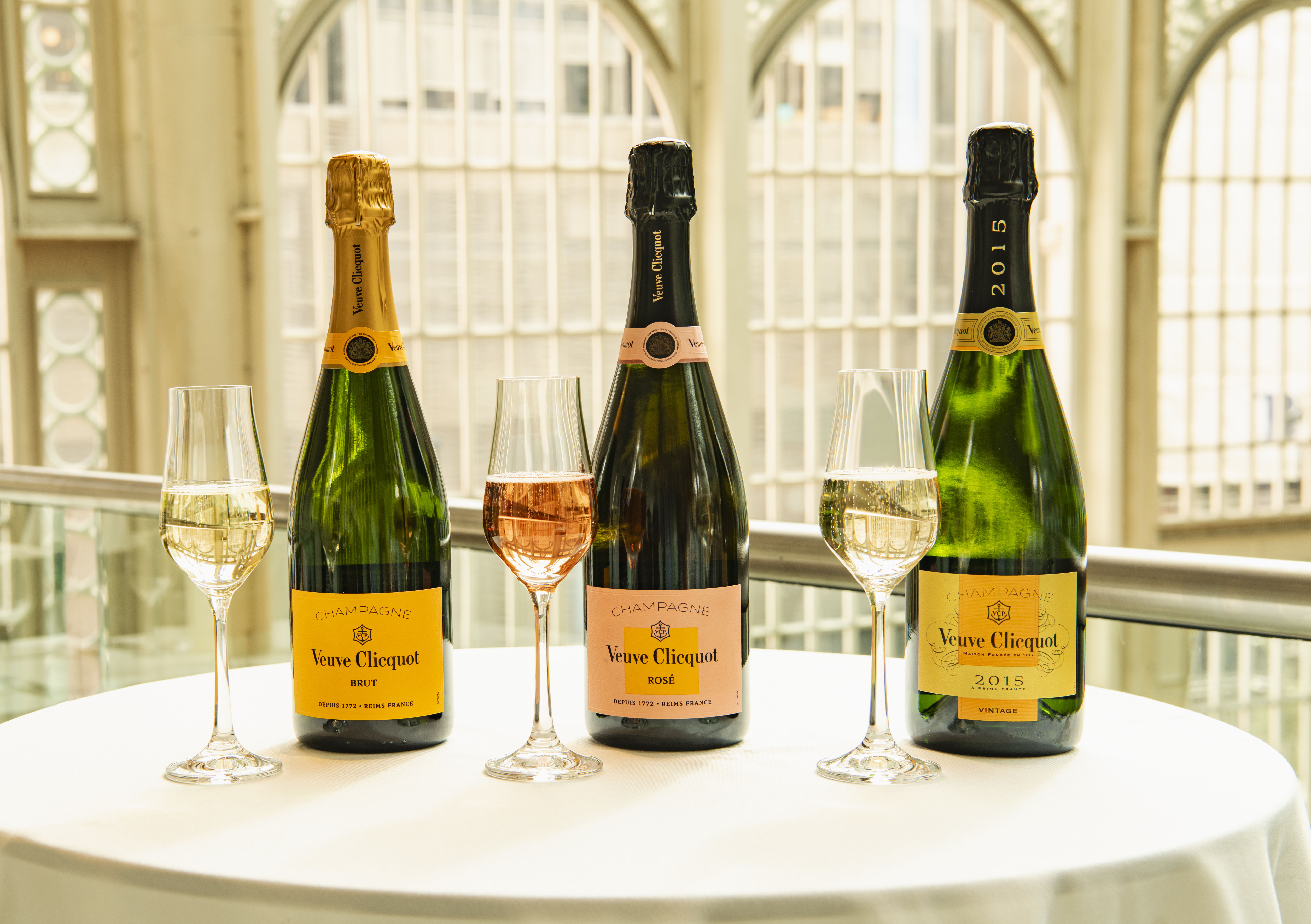 Three bottles of Veuve Clicquot champagne are lined up on a table with glasses in front of them.