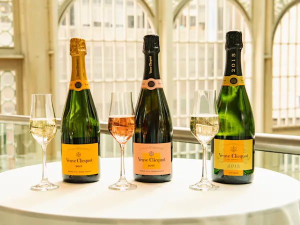 Three bottles of Veuve Clicquot champagne are lined up on a table with glasses in front of them.