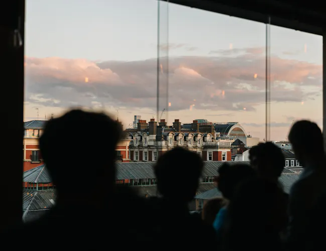 A group of people are in a shadow looking out over the piazza of Covent Garden. They are on the Cicoria Terrace within the Royal Opera House for a Young RBO night. (3 of 9)