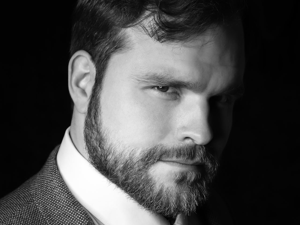 A black and white headshot of the opera singer Aleksei Isaev. He wears a great suit, black tie and white shirt and has a beard.