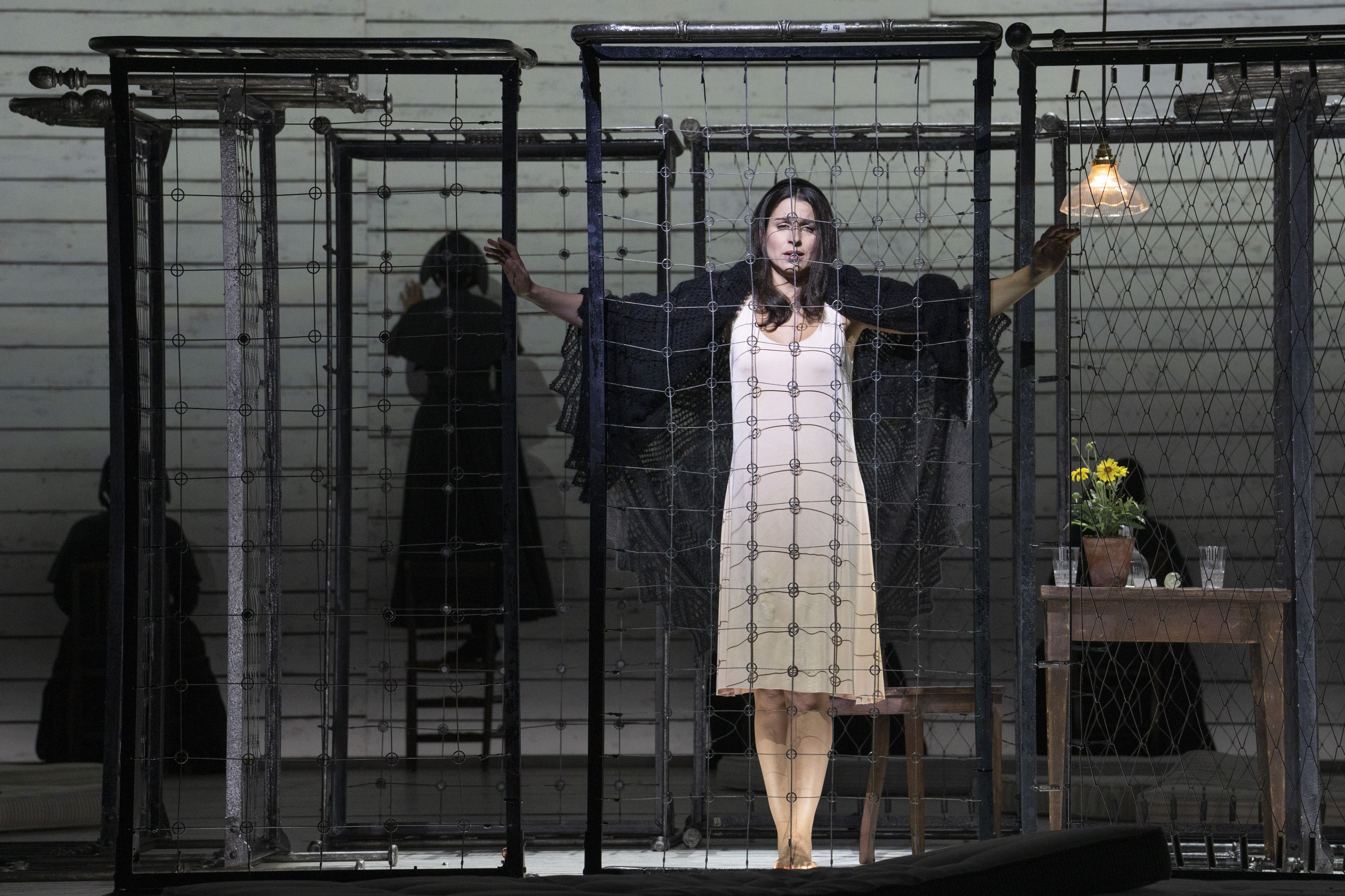 A woman in a white dress stands in a cage. 