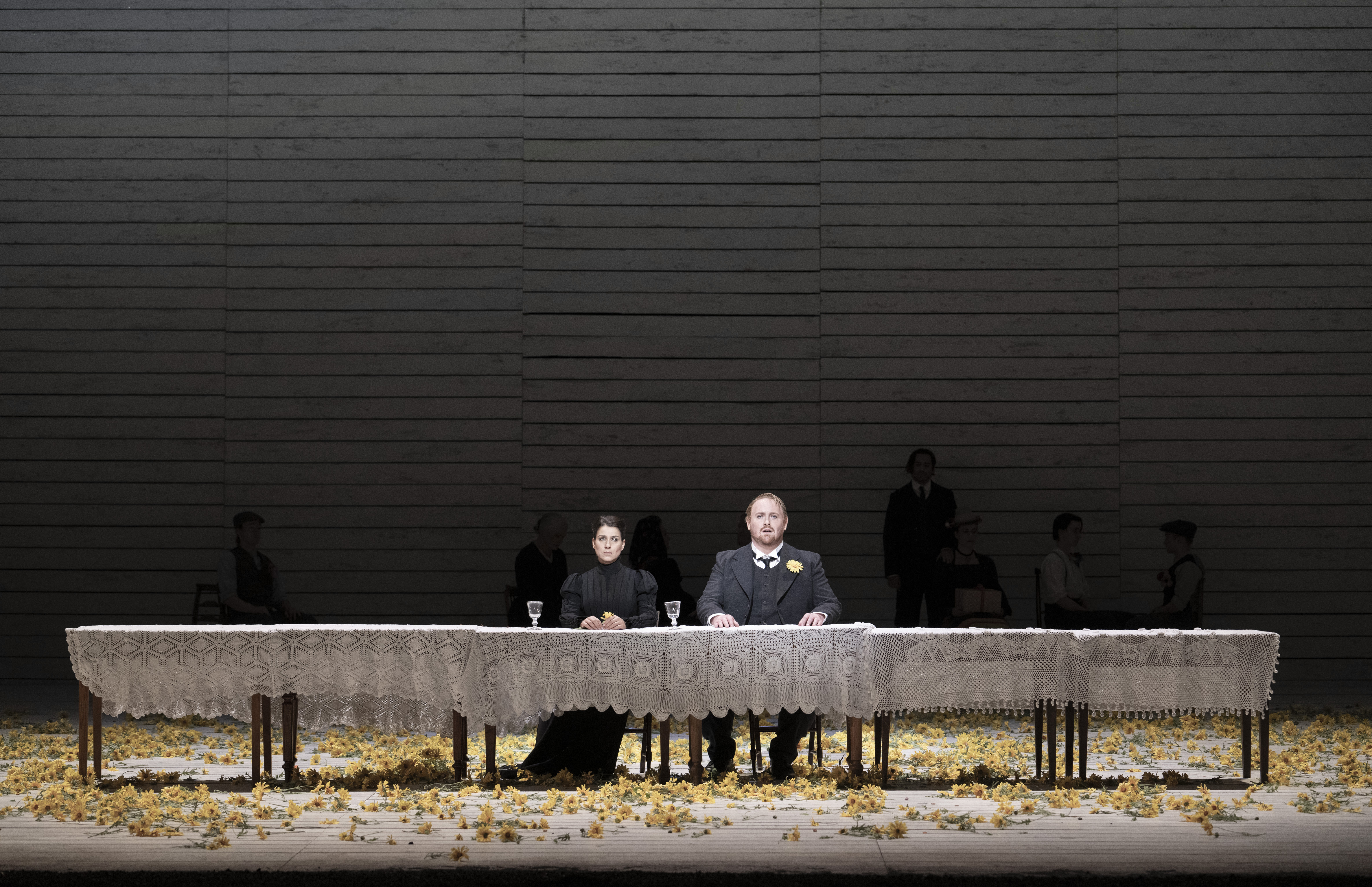 Two woman sit at a long table covered in a white tablecloth. 