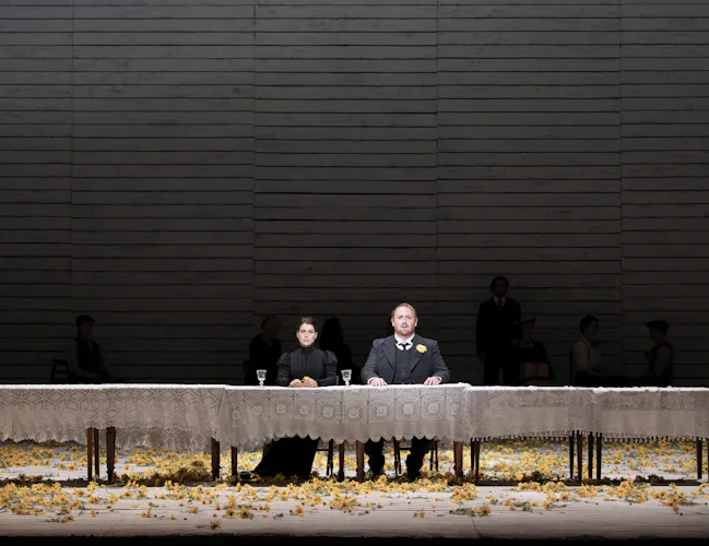 Two woman sit at a long table covered in a white tablecloth.
