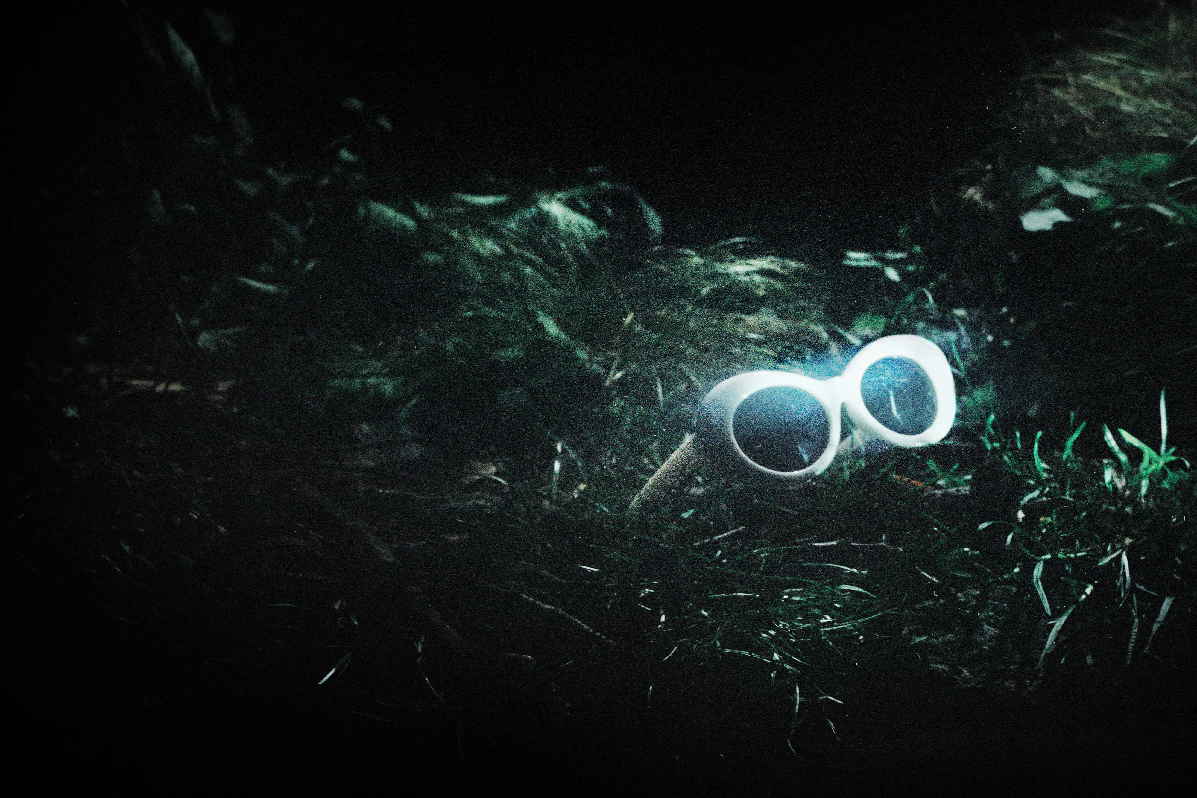 A pair of white 60s style framed sunglasses sit in amongst green grass. They represent the glasses worn by Kurt Cobain in The Royal Opera’s production of Last Days.  