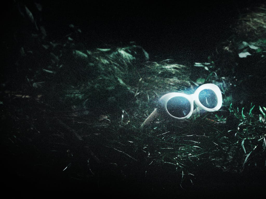 A pair of white 60s style framed sunglasses sit in amongst green grass. They represent the glasses worn by Kurt Cobain in The Royal Opera’s production of Last Days.