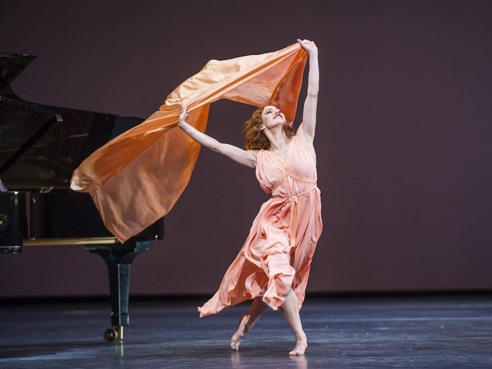 A dancer waves an orange scarf overhead in a performance of The Dream / Short Works / Rhapsody. 
