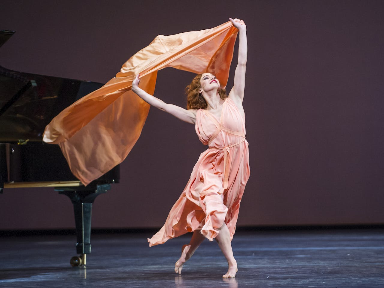 A dancer waves an orange scarf overhead in a performance of The Dream / Short Works / Rhapsody. 