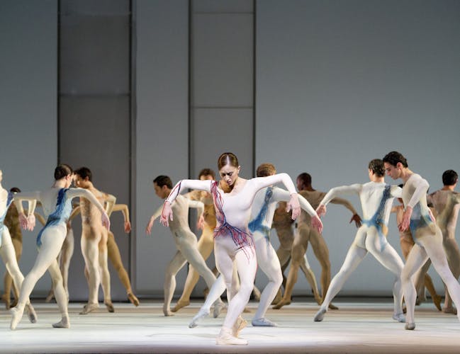 Dancers in white costumes stand still on stage