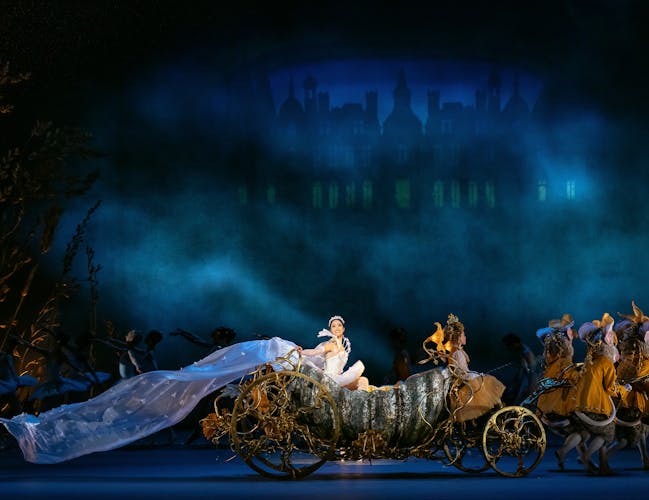 An elaborate carriage sits in the centre of the stage as a performer in a ballgown looks out at the audience.