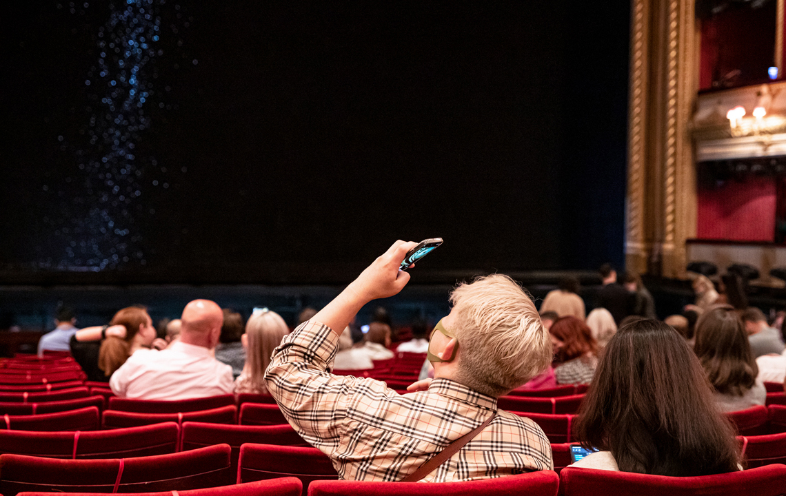 A person takes a photo on their phone inside the Royal Opera House main auditorium. 