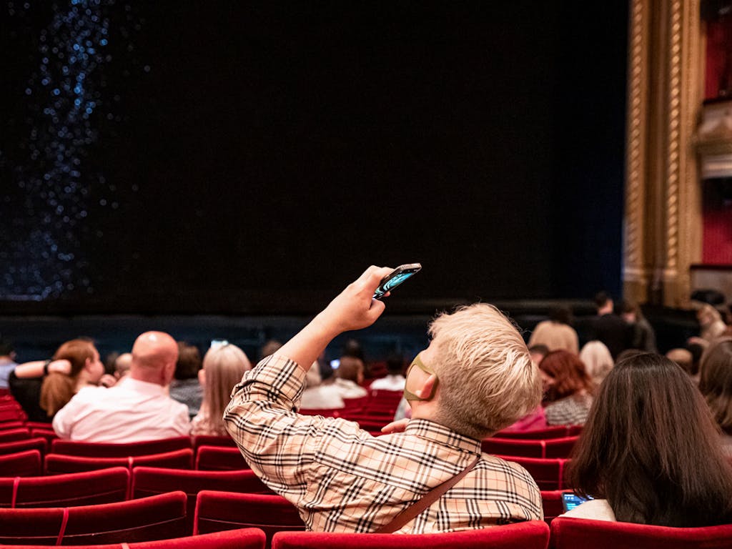 A person takes a photo on their phone inside the Royal Opera House main auditorium. 