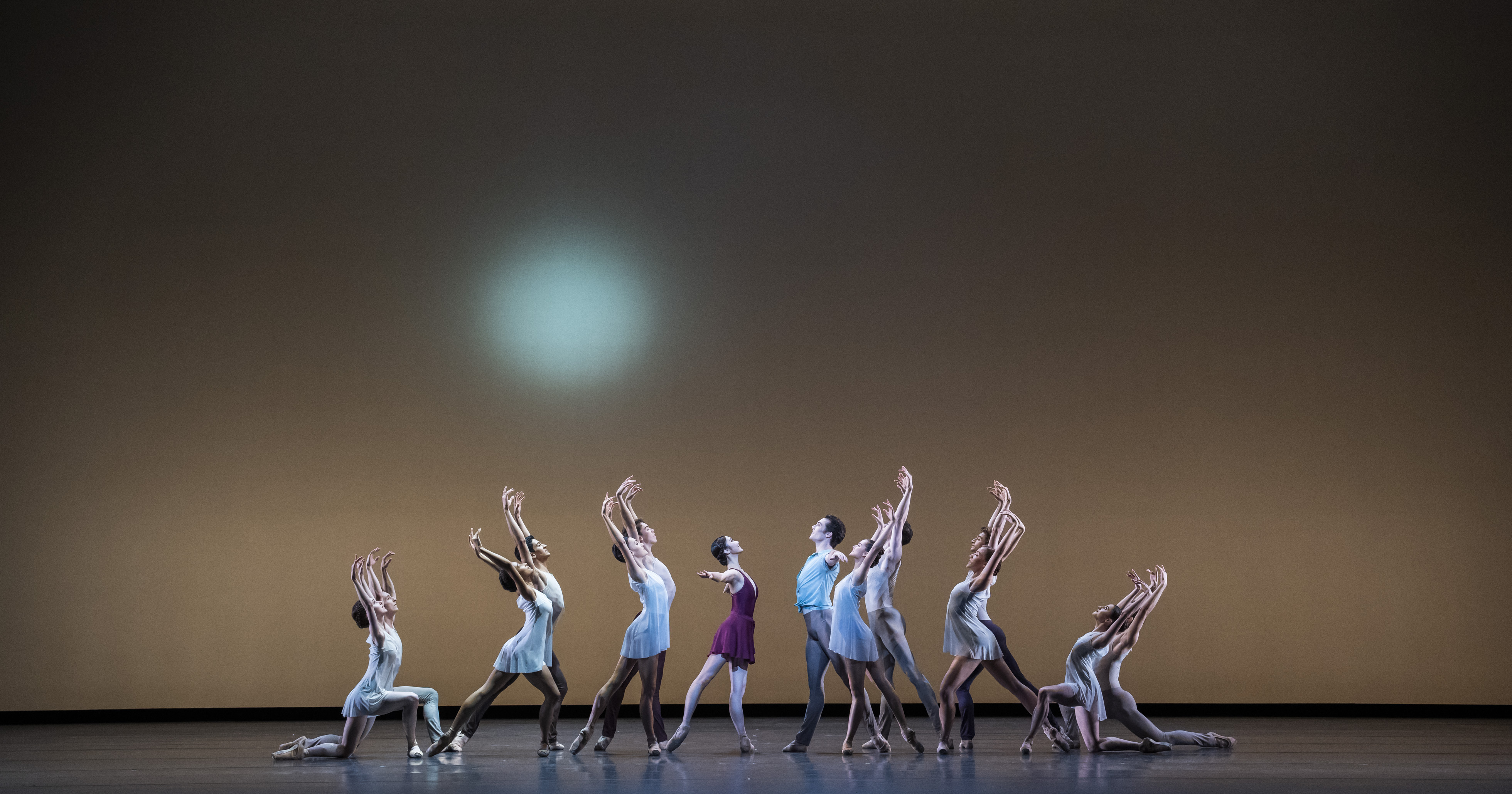 A group of dancers in a triangle formation, standing in arabesque with their arms raised above their heads. (2 of 3)