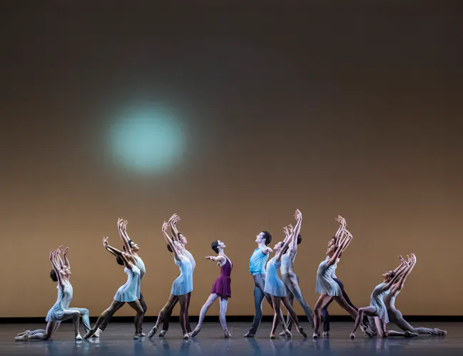 A group of dancers in a triangle formation, standing in arabesque with their arms raised above their heads. (2 of 3)