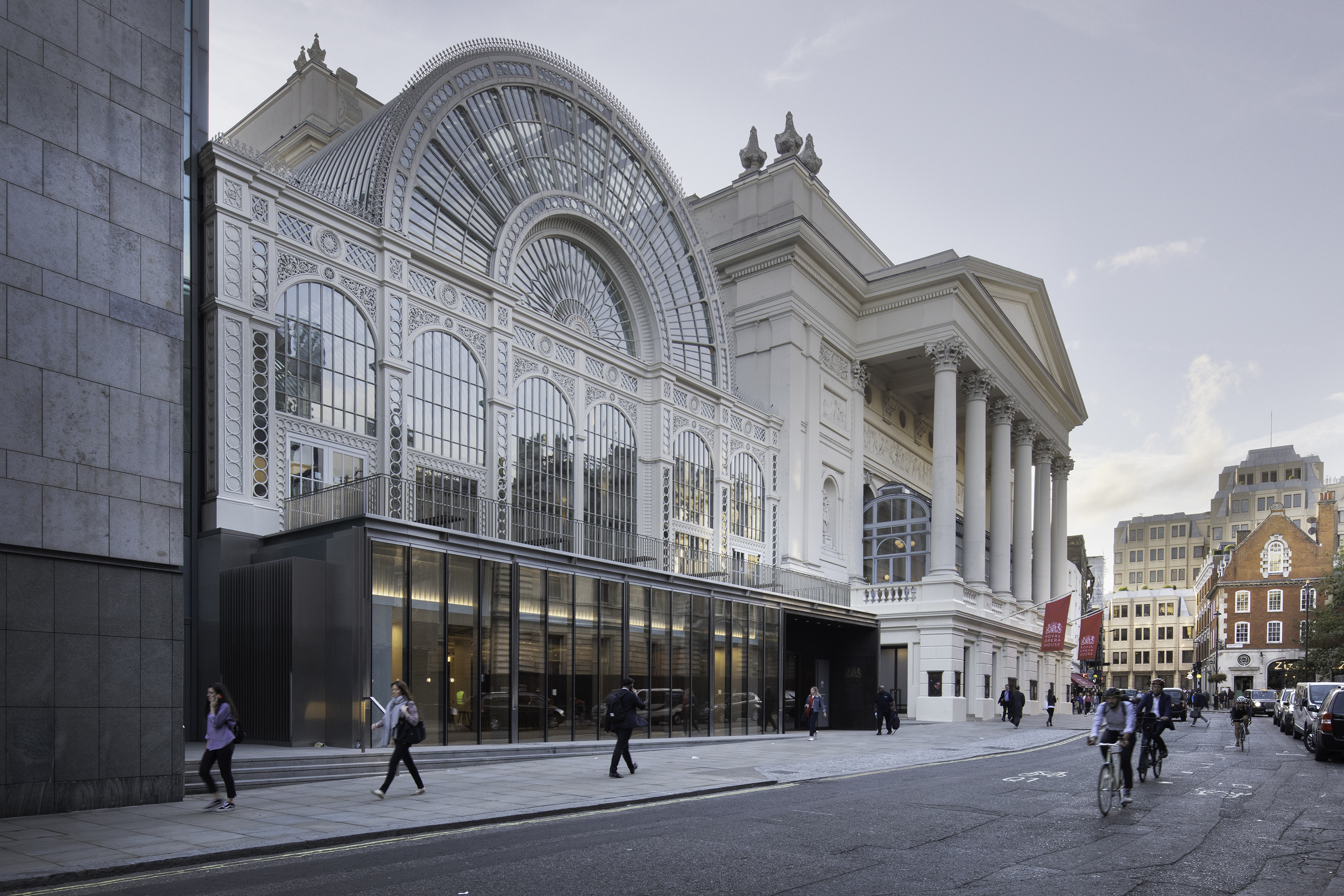 An image of the Royal Opera House from Bow Street - a large glass fronted building next to a traditional building with six columns