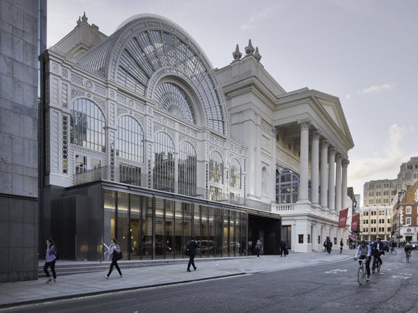 An image of the Royal Opera House from Bow Street - a large glass fronted building next to a traditional building with six columns