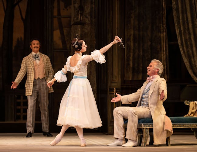 Female dancer reaches out to seated male dancer in period costume.