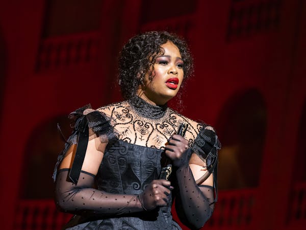 A woman in a black dress holding a fan looks out onto the audience from the stage as she sings.