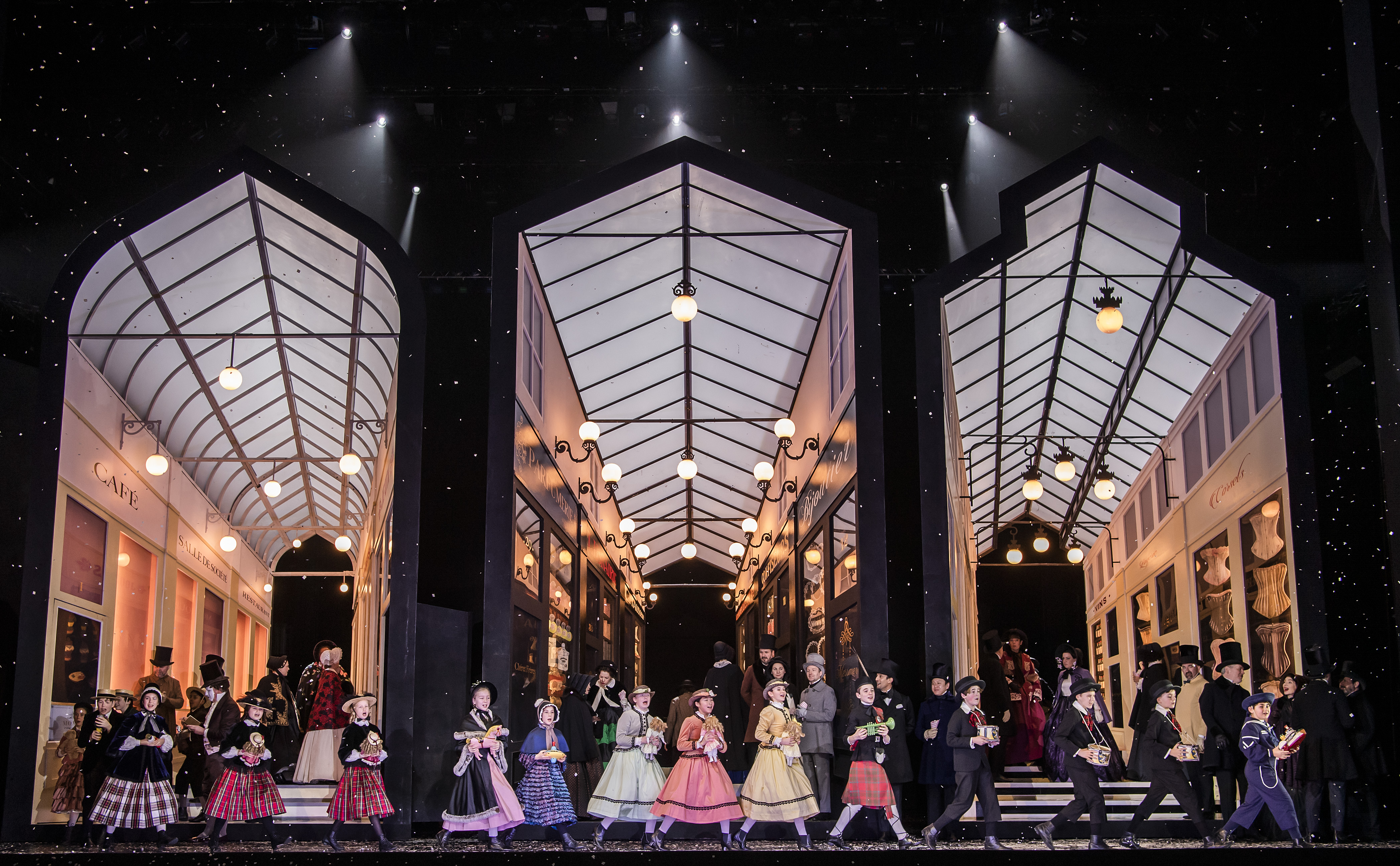 A large set of three arcades appear on stage. In front of the set children hold presents and sing, they are wearing colourful dresses. (2 of 4)